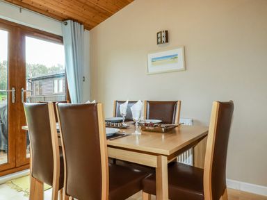 A dining room with six brown leather chairs around a wooden table set for a meal at 4 The Glade in St Minver