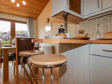 A kitchen with wooden stools and countertop with food next to a dining table and chairs at 4 The Glade in St Minver