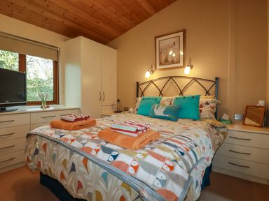A bedroom with a double bed blue pillows folded towels bedside cabinets and a television at 4 The Glade in St Minver