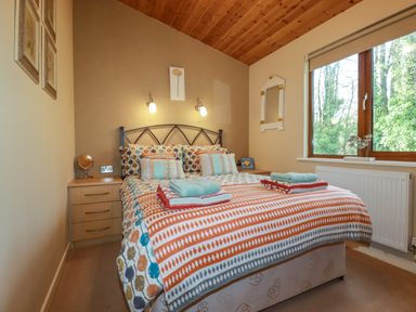A bedroom with a double bed dressed in patterned bedding with two bedside tables and a window at 4 The Glade in St Minver
