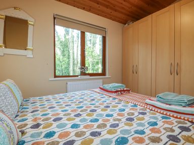 A bedroom with a patterned bedspread folded towels a window and wooden wardrobes at 4 The Glade in St Minver