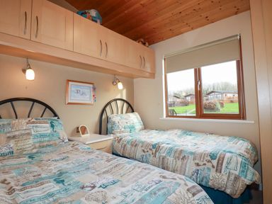 A bedroom with two single beds and a window showing a view of cabins at 4 The Glade in St Minver