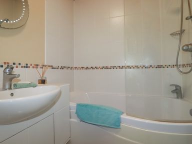 A bathroom with a white sink and cabinet a bathtub with a shower and a turquoise towel hanging at 4 The Glade in St Minver