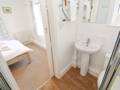 A bedroom with a bed and window next to a small bathroom with a sink mirror and towel rack at Godrevy in Porthcurno