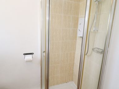 A shower area with a glass door a showerhead control panel and tiled walls at Godrevy in Porthcurno