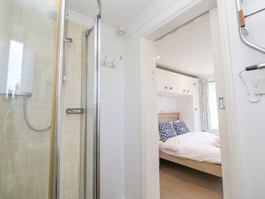 A view from a bathroom with a shower into a bedroom with a bed and overhead cabinets at Godrevy in Porthcurno
