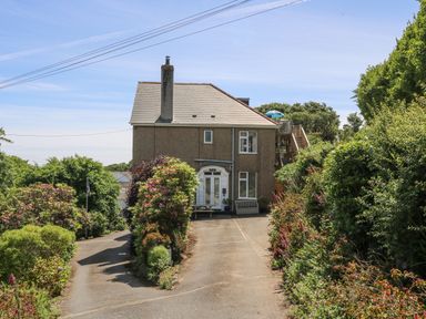 A two-story house with a driveway surrounded by bushes and flowers at Godrevy in Porthcurno