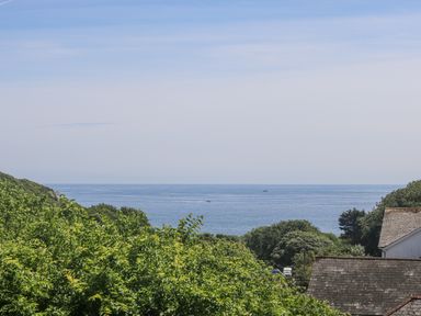 A view of the ocean with trees and rooftops in the foreground at Godrevy in Porthcurno