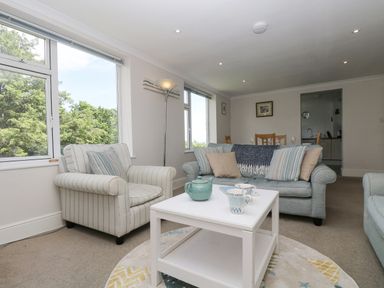 A living room with a striped armchair a sofa with cushions and a white coffee table with a teapot at Godrevy in Porthcurno