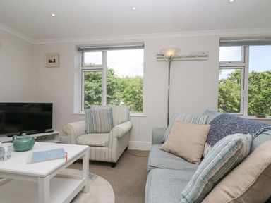 A living room with a sofa and armchair with striped cushions a coffee table and a television at Godrevy in Porthcurno