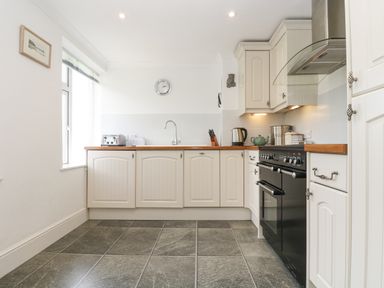 A kitchen with cream cabinets a black oven wooden countertops and a window at Godrevy in Porthcurno