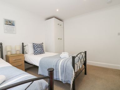 A bedroom with two single beds a wooden nightstand with lamps a white wardrobe and a framed picture on the wall at Godrevy in Porthcurno