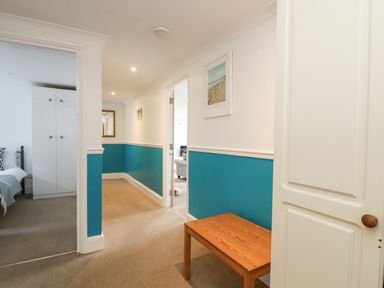 A hallway with teal and white walls a wooden bench and open doors leading to a bedroom and living room at Godrevy in Porthcurno