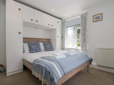 A bedroom with a double bed with blue and white pillows and a blue blanket under white cabinets at Godrevy in Porthcurno