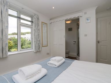 A bedroom with a bed with folded towels a window with curtains and an en suite bathroom at Godrevy in Porthcurno