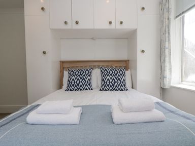 A bedroom with a wooden bed headboard blue patterned pillows white towels and built in cabinets at Godrevy in Porthcurno
