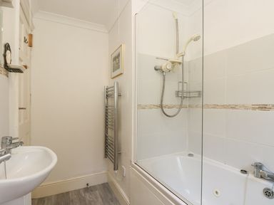 A bathroom with a bathtub and shower combination a sink a wall-mounted towel radiator and a framed picture at Godrevy in Porthcurno