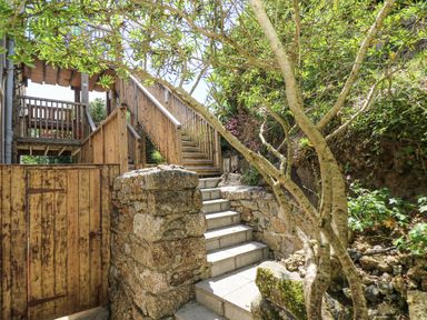 Stone steps leading to a wooden staircase and gate surrounded by trees and plants at Godrevy in Porthcurno