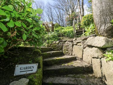 Stone steps with moss and a garden sign surrounded by plants and trees at Godrevy in Porthcurno