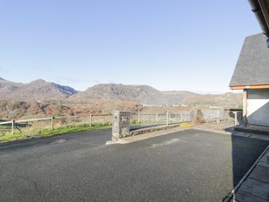 An asphalt driveway with a stone pillar and metal railing overlooking hills at Y Tylwyth in Blaenau Ffestiniog