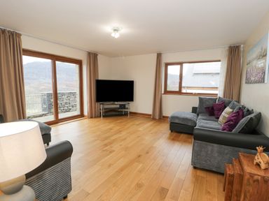 A living room with a corner sofa with cushions a television on a stand wooden floors and large windows at Y Tylwyth in Blaenau Ffestiniog