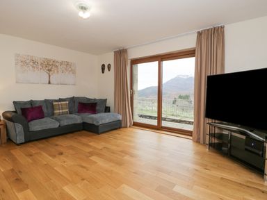 A living room with a grey sofa and a large window showing a mountain view at Y Tylwyth in Blaenau Ffestiniog