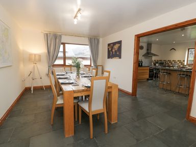 A dining area with a wooden table set with plates and glasses next to a kitchen with bar stools at Y Tylwyth in Blaenau Ffestiniog