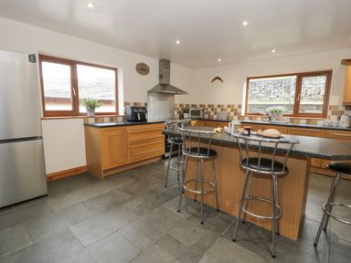 A kitchen with wooden cabinets a black countertop a stainless steel refrigerator stove and three metal bar stools at Y Tylwyth in Blaenau Ffestiniog