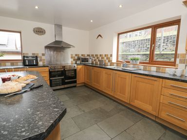 A kitchen with wooden cabinets black countertops double oven microwave and large windows at Y Tylwyth in Blaenau Ffestiniog