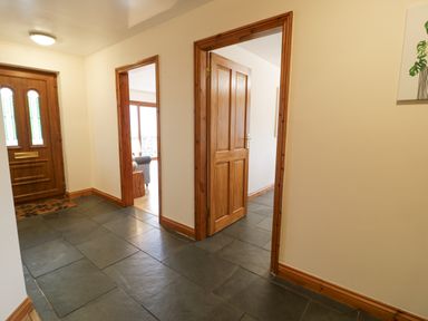 A hallway with dark tile floor wooden doors and a wooden front door at Y Tylwyth in Blaenau Ffestiniog