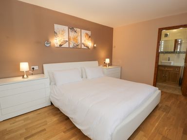 A bedroom with a white bed flanked by two white bedside tables with lamps and a door leading to a bathroom at Y Tylwyth in Blaenau Ffestiniog