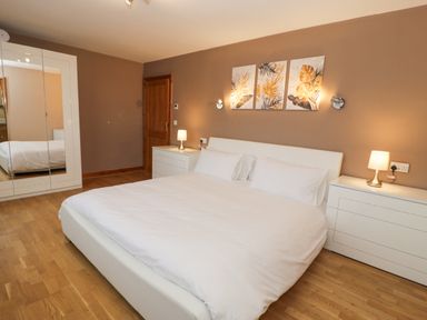 A bedroom with a large white bed two white dressers lamps and three framed pictures on the wall at Y Tylwyth in Blaenau Ffestiniog