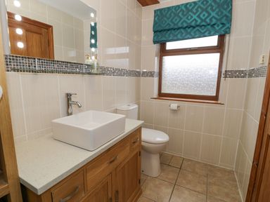 A bathroom with a wooden vanity unit with a square sink a toilet a window with a teal blind and tiled walls at Y Tylwyth in Blaenau Ffestiniog