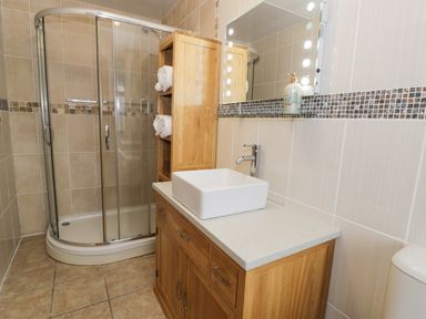 A bathroom with a wooden vanity with a square sink a glass shower enclosure and a wooden shelving unit with towels at Y Tylwyth in Blaenau Ffestiniog