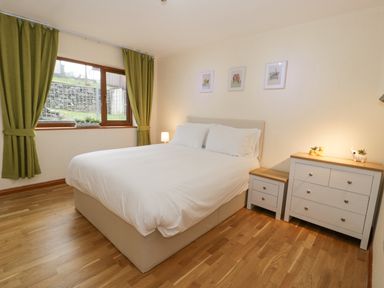 A bedroom with a large bed white bedding wooden floor and green curtains at Y Tylwyth in Blaenau Ffestiniog