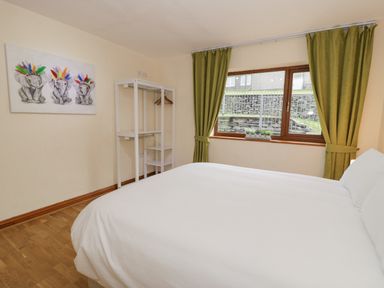 A bedroom with a bed a window with green curtains a white open wardrobe and a painting of elephants on the wall at Y Tylwyth in Blaenau Ffestiniog