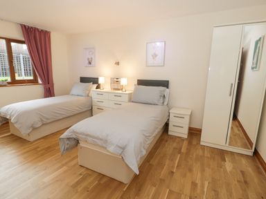 A bedroom with two single beds a nightstand a dresser with lamps a wardrobe and a window with curtains at Y Tylwyth in Blaenau Ffestiniog