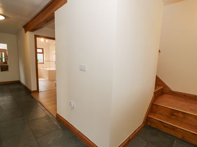 A hallway with stone tile flooring wooden staircase and a view into a bathroom at Y Tylwyth in Blaenau Ffestiniog