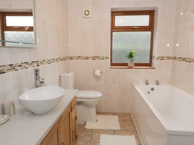 A bathroom with a sink on a wooden cabinet a toilet a bathtub and a window with a plant at Y Tylwyth in Blaenau Ffestiniog