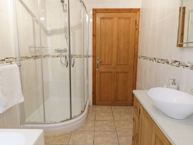 A bathroom with a glass shower enclosure a wooden door a sink on a wooden cabinet and a towel on a rack at Y Tylwyth in Blaenau Ffestiniog