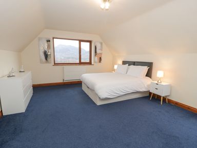 A bedroom with a bed two bedside tables with lamps a chest of drawers and a window showing a mountain view at Y Tylwyth in Blaenau Ffestiniog