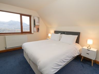 A bedroom with a bed white bedding bedside tables with lamps a window and a painting on the wall at Y Tylwyth in Blaenau Ffestiniog