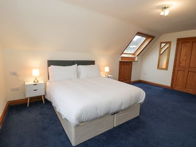 A bedroom with a double bed bedside tables lamps a window mirror and wooden doors at Y Tylwyth in Blaenau Ffestiniog