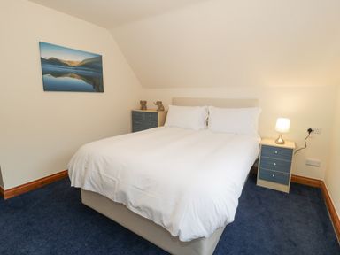 A bedroom with a double bed white bedding two bedside tables with drawers and a lamp two elephant figurines on a chest of drawers and a landscape picture on the wall at Y Tylwyth in Blaenau Ffestiniog
