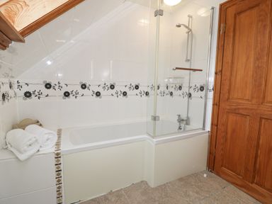 A bathroom with a bathtub and shower with floral tile border and wooden door at Y Tylwyth in Blaenau Ffestiniog