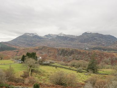 A rural landscape with green fields trees and mountains under a cloudy sky at Y Tylwyth in Blaenau Ffestiniog