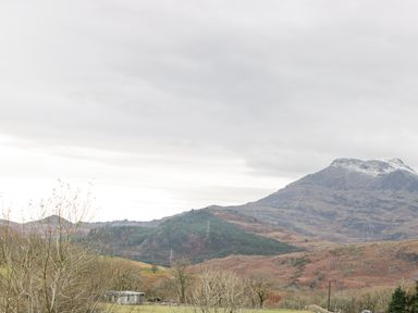 Mountains with patches of snow above a landscape with trees a small building and power lines at Y Tylwyth in Blaenau Ffestiniog