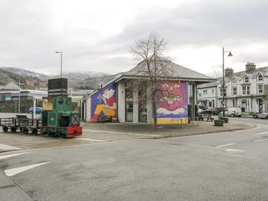 A street corner with a small green train and colorful murals on a building at Y Tylwyth in Blaenau Ffestiniog