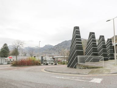 An outdoor area with black striped stone pillars and railings near a roundabout with mountains in the background at Y Tylwyth in Blaenau Ffestiniog