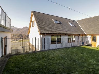 A fenced yard with grass and a house with a sloped roof and windows at Y Tylwyth in Blaenau Ffestiniog